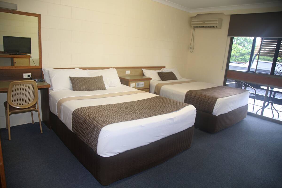 A hotel room with two beds, a desk, a chair, and a large window with a view.