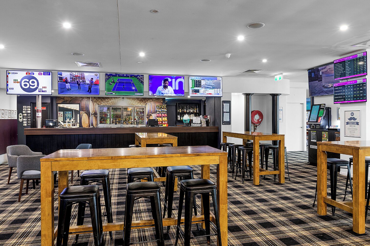 A bar area with multiple screens displaying sports events, wooden tables and stools, and a counter with various items.