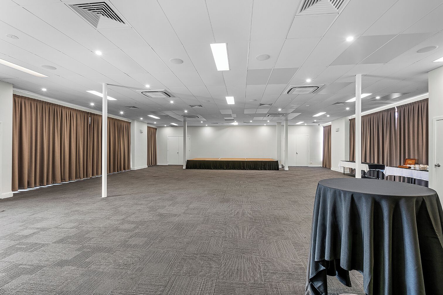 Un amplio salón de conferencias con techo alto, piso alfombrado y una larga mesa cubierta con mantel.
