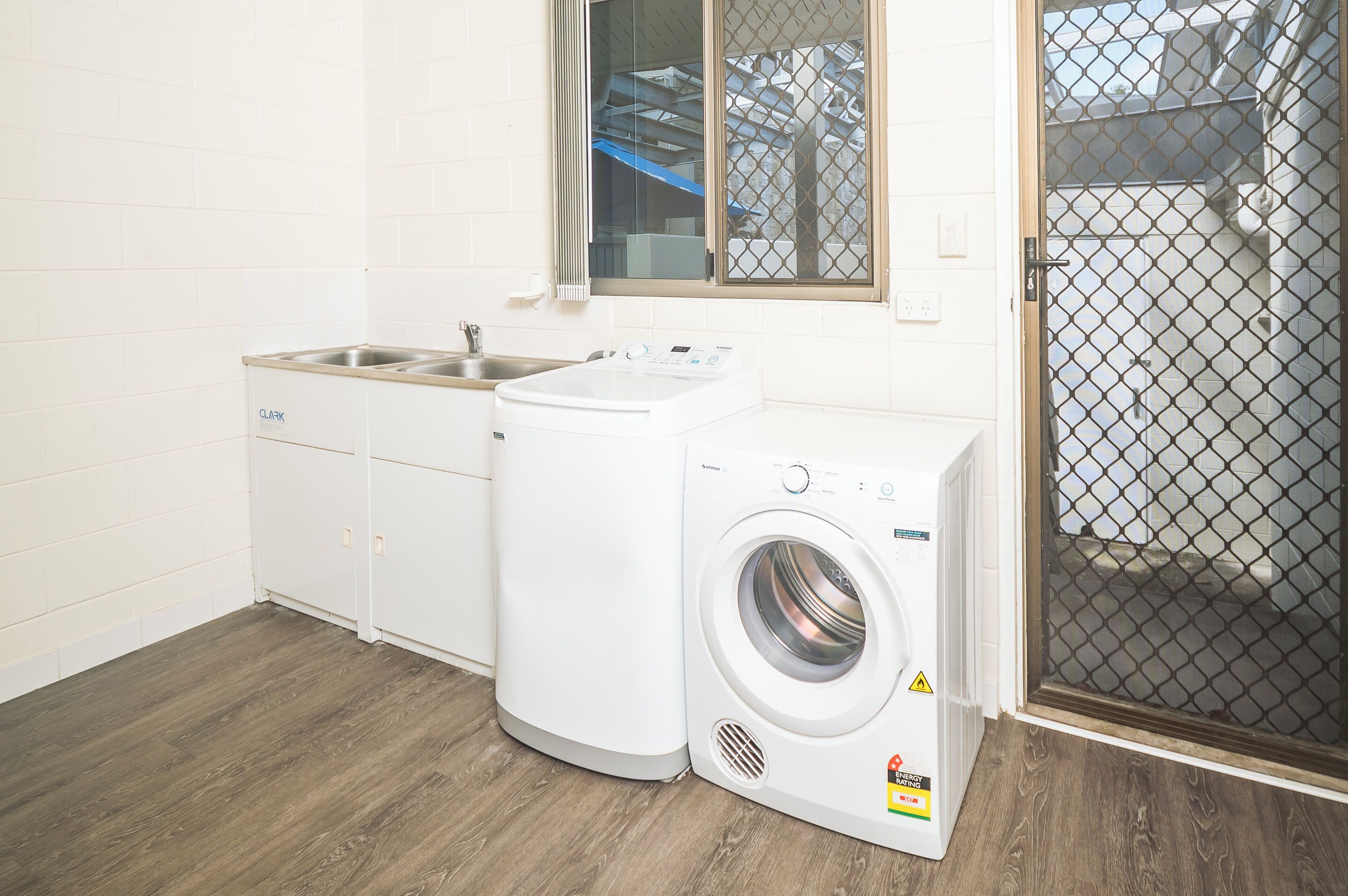 Une buanderie équipée d’un lave-linge, d’un évier et d’une fenêtre donnant sur un immeuble.