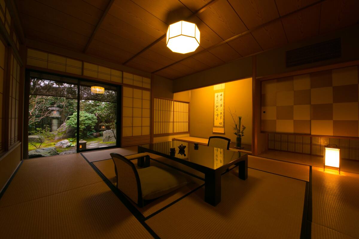 A traditional Japanese room with tatami flooring, a low table, and sliding doors leading to a garden.