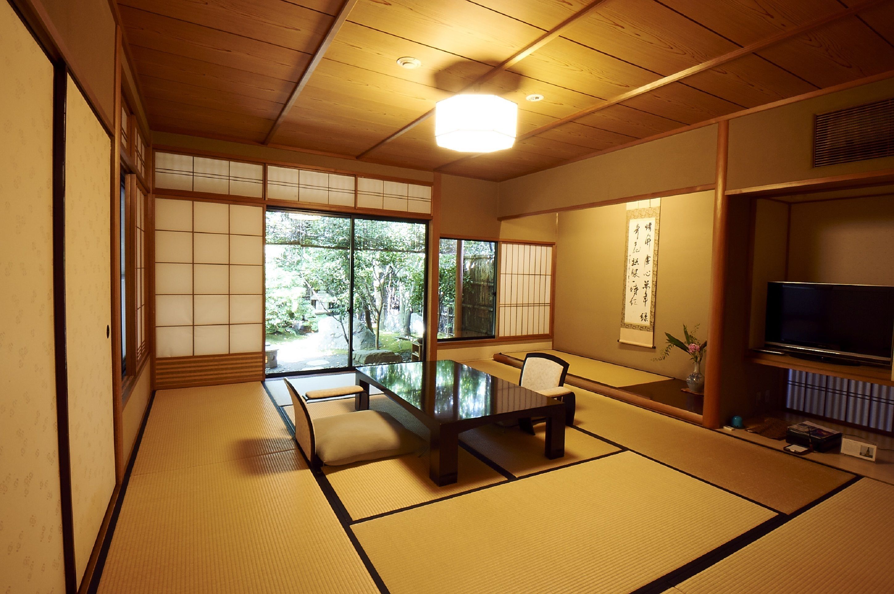 A traditional Japanese room with tatami flooring, a low table, a chair, sliding doors, and a television.