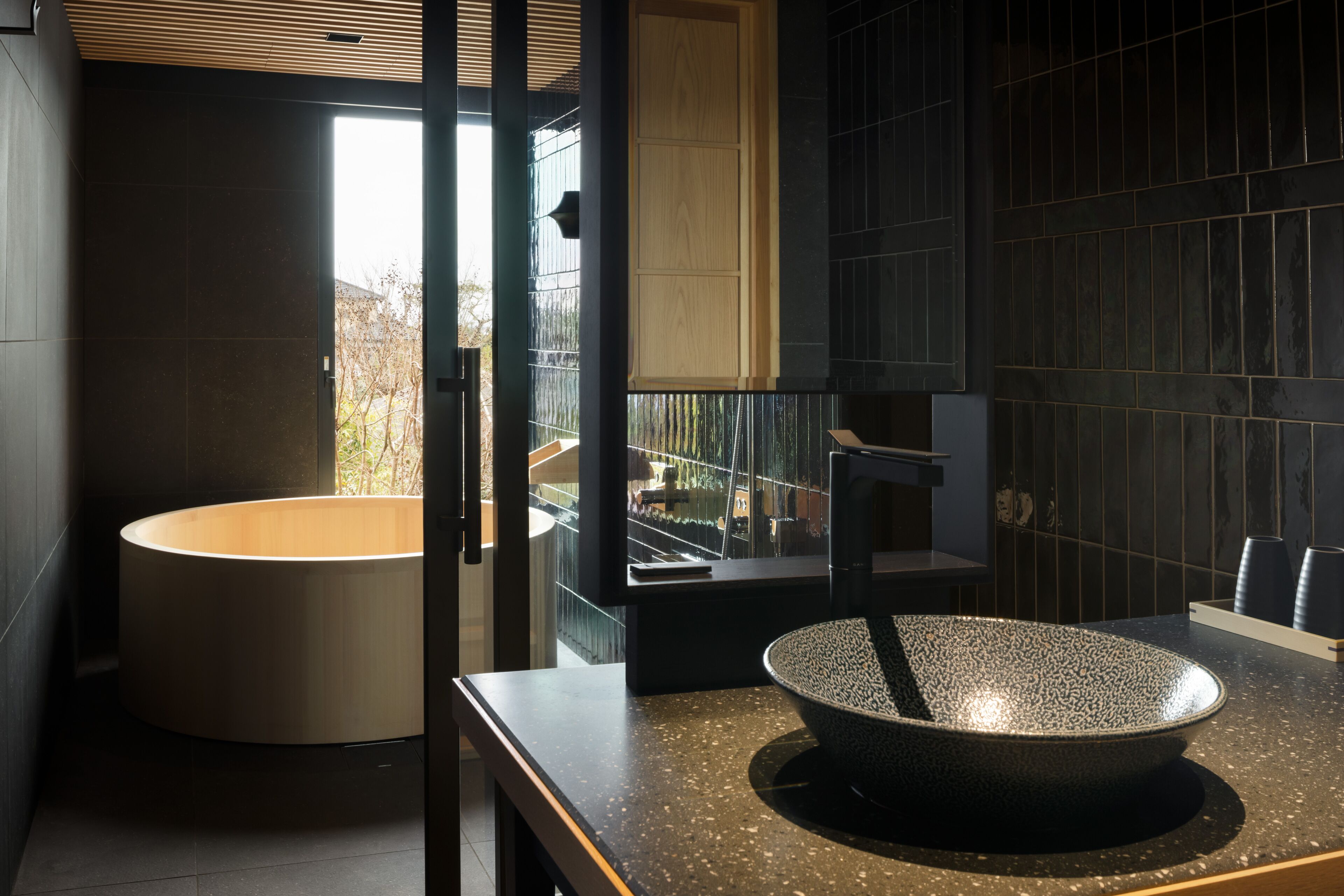 A modern bathroom with a freestanding bathtub, a large bowl sink, and a view of the outdoors through a glass door.
