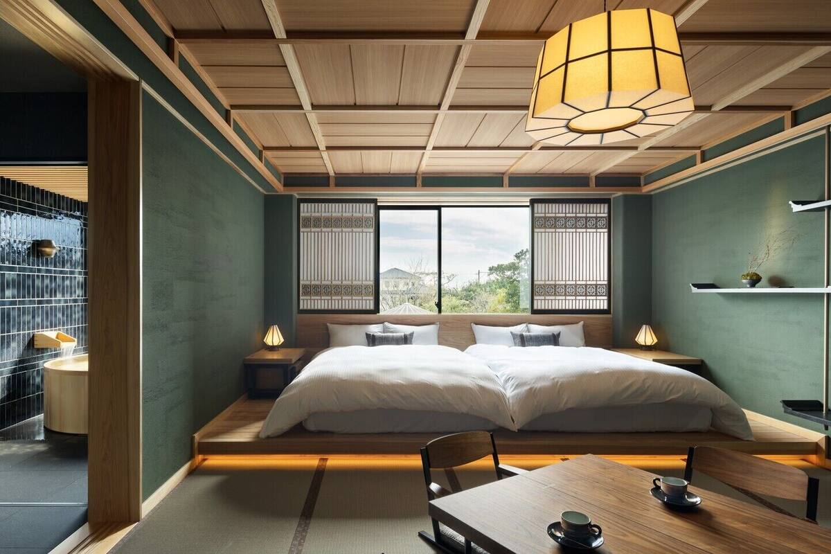 A modern bedroom with a wooden ceiling, a large bed, bedside tables, a TV, and a view through the window.