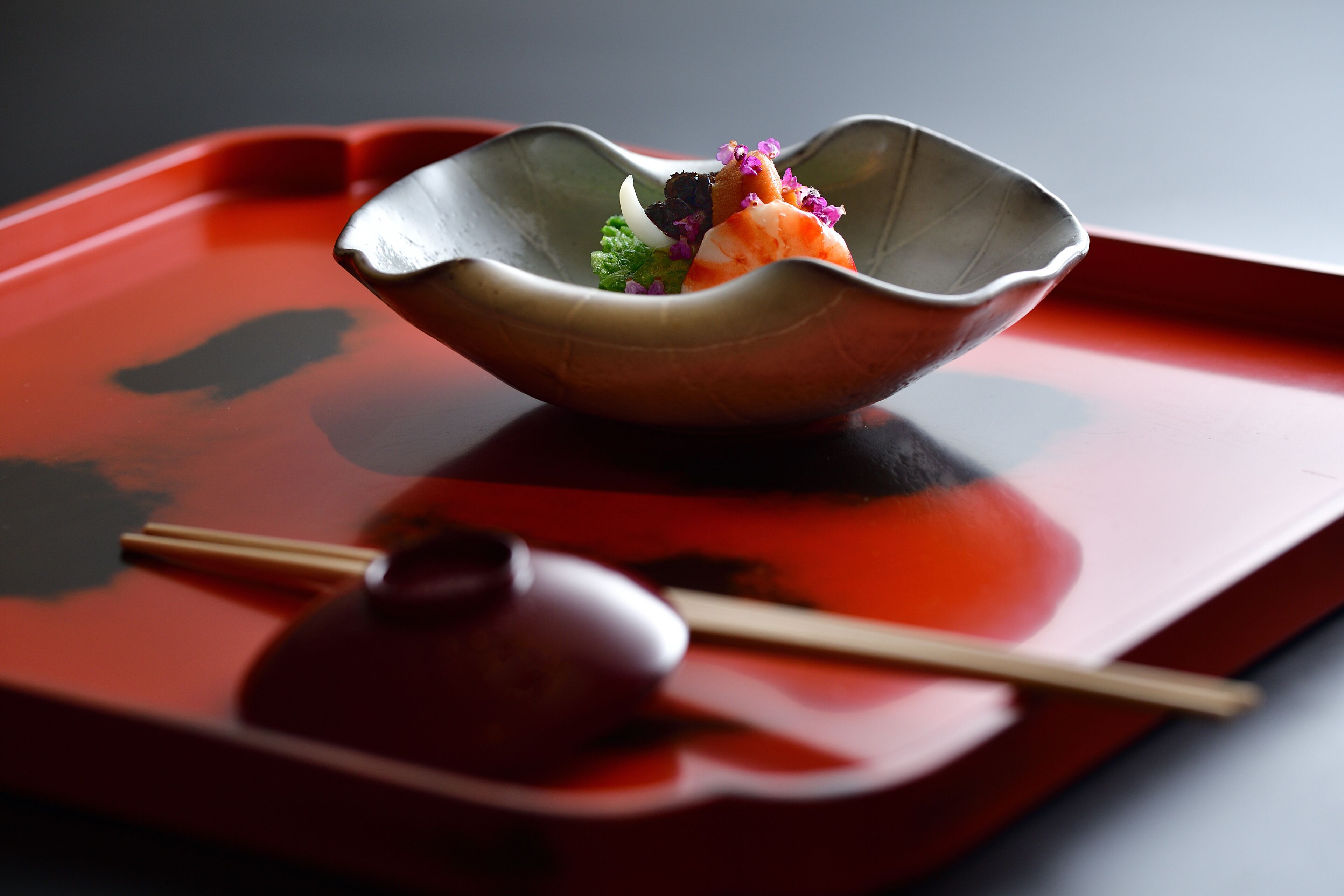 A bowl of food on a red tray with chopsticks and a small item beside it.