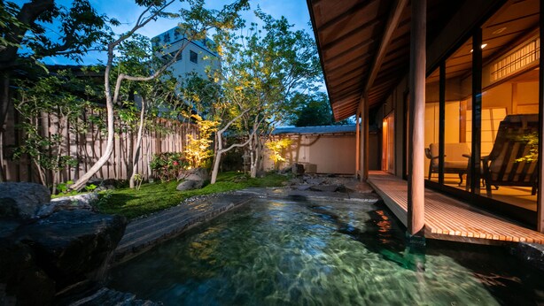 A serene outdoor area with a clear water feature, wooden deck, and a building with large windows. - Yakakutei (Kirishima)