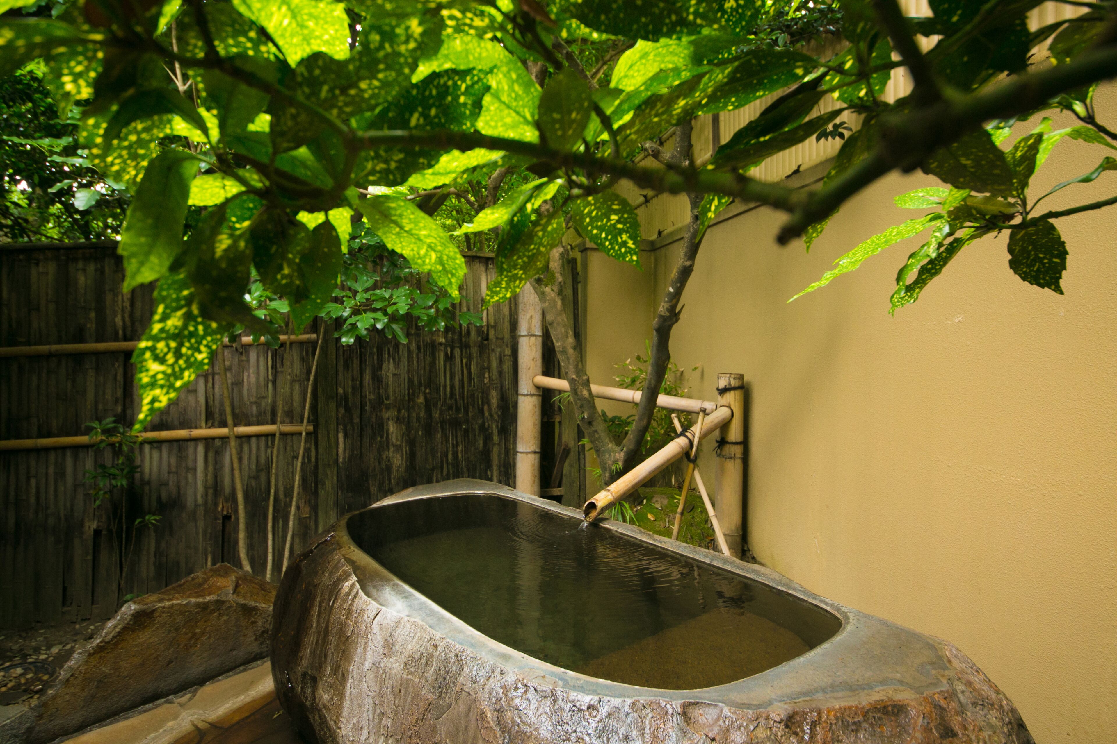 Un bain traditionnel en pierre chauffé par des sources chaudes, doté d’une structure en bambou, entouré d’une clôture en bois et d’une végétation luxuriante.