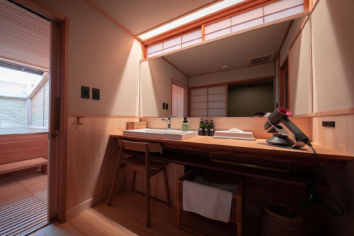 Een kleine badkamer met een houten wastafelmeubel, een spiegel en een haardroger.