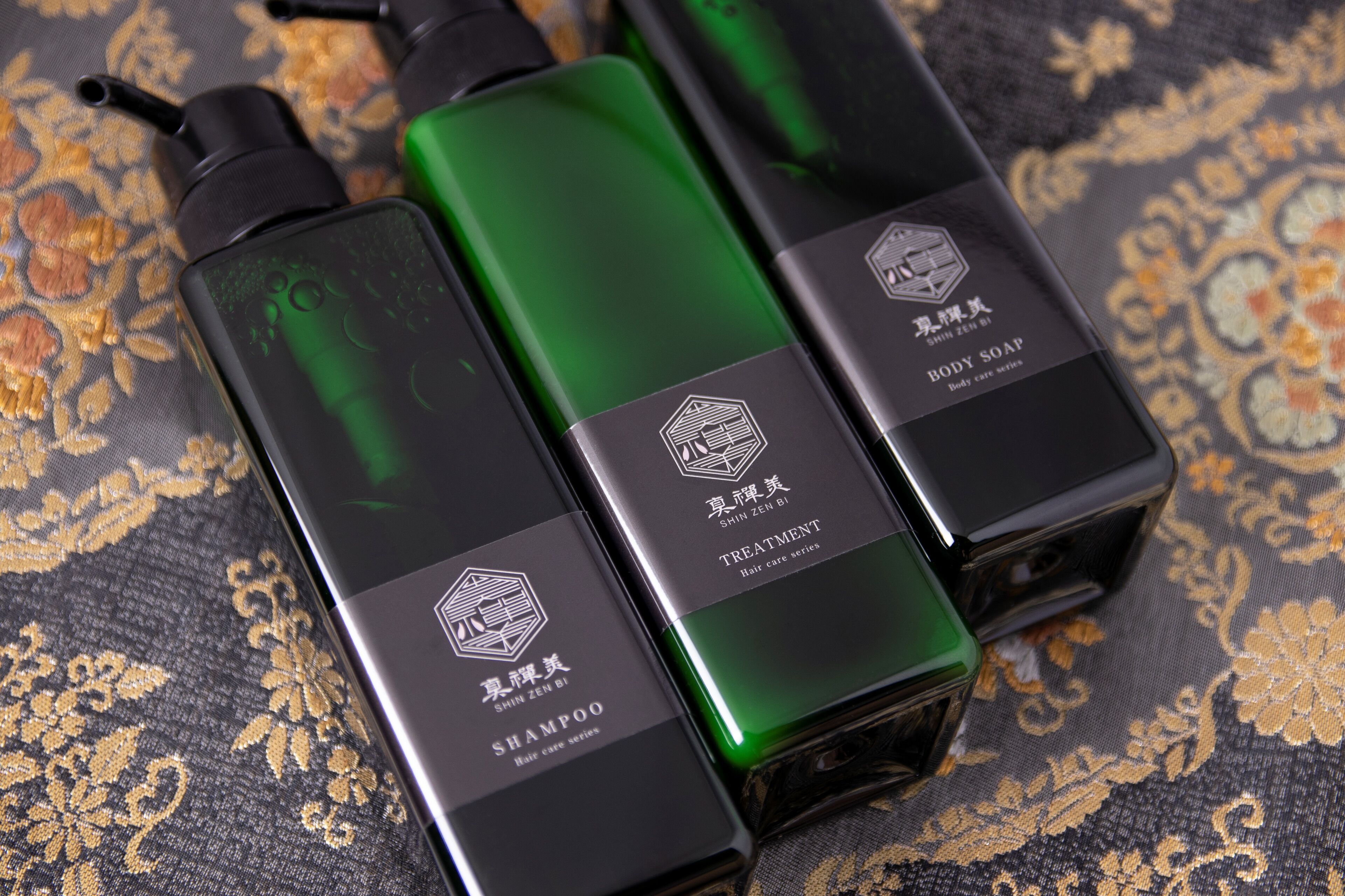 Three bottles of body care products on a patterned fabric surface.