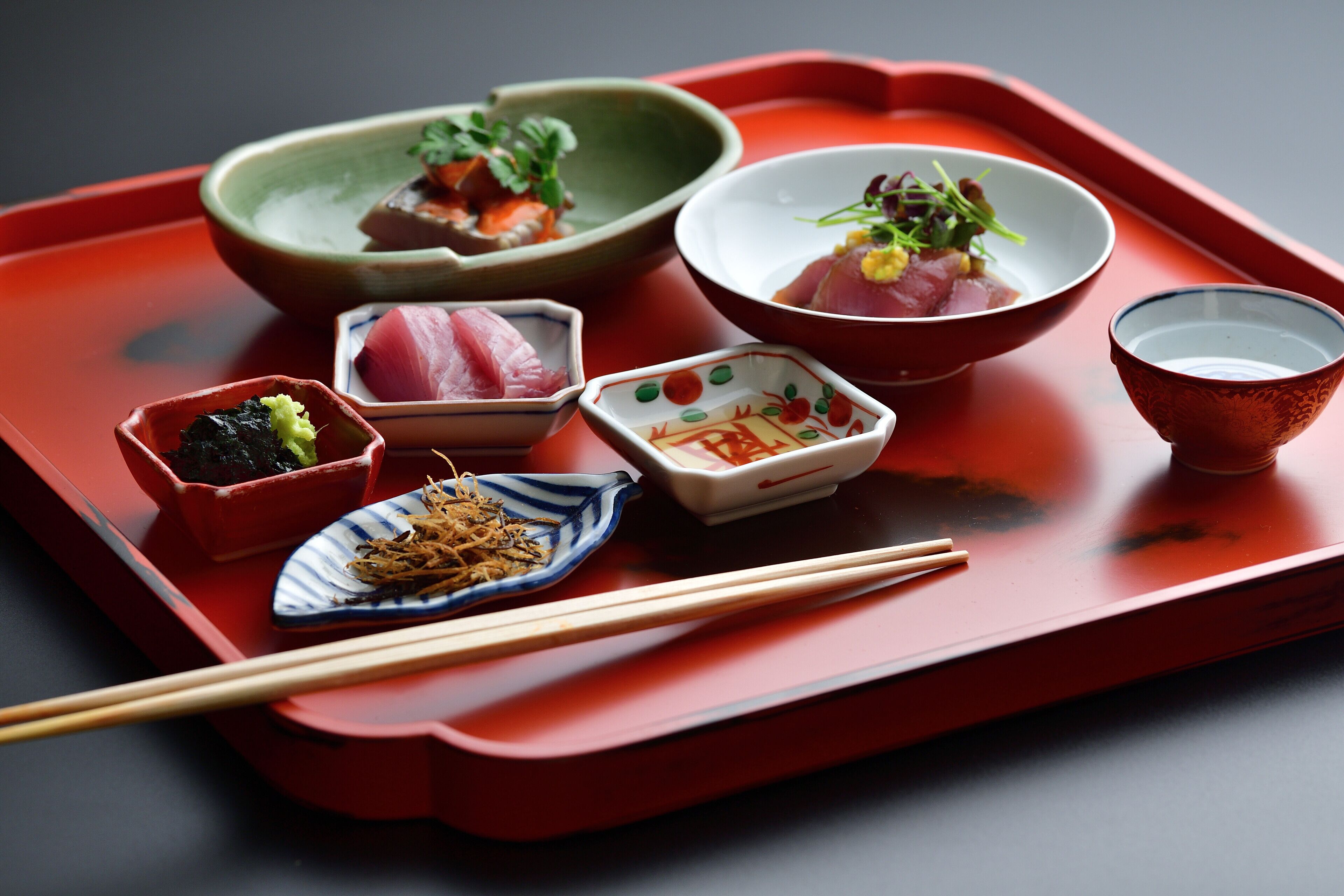 A tray with various Japanese dishes, including sashimi and vegetables, and a pair of chopsticks.
