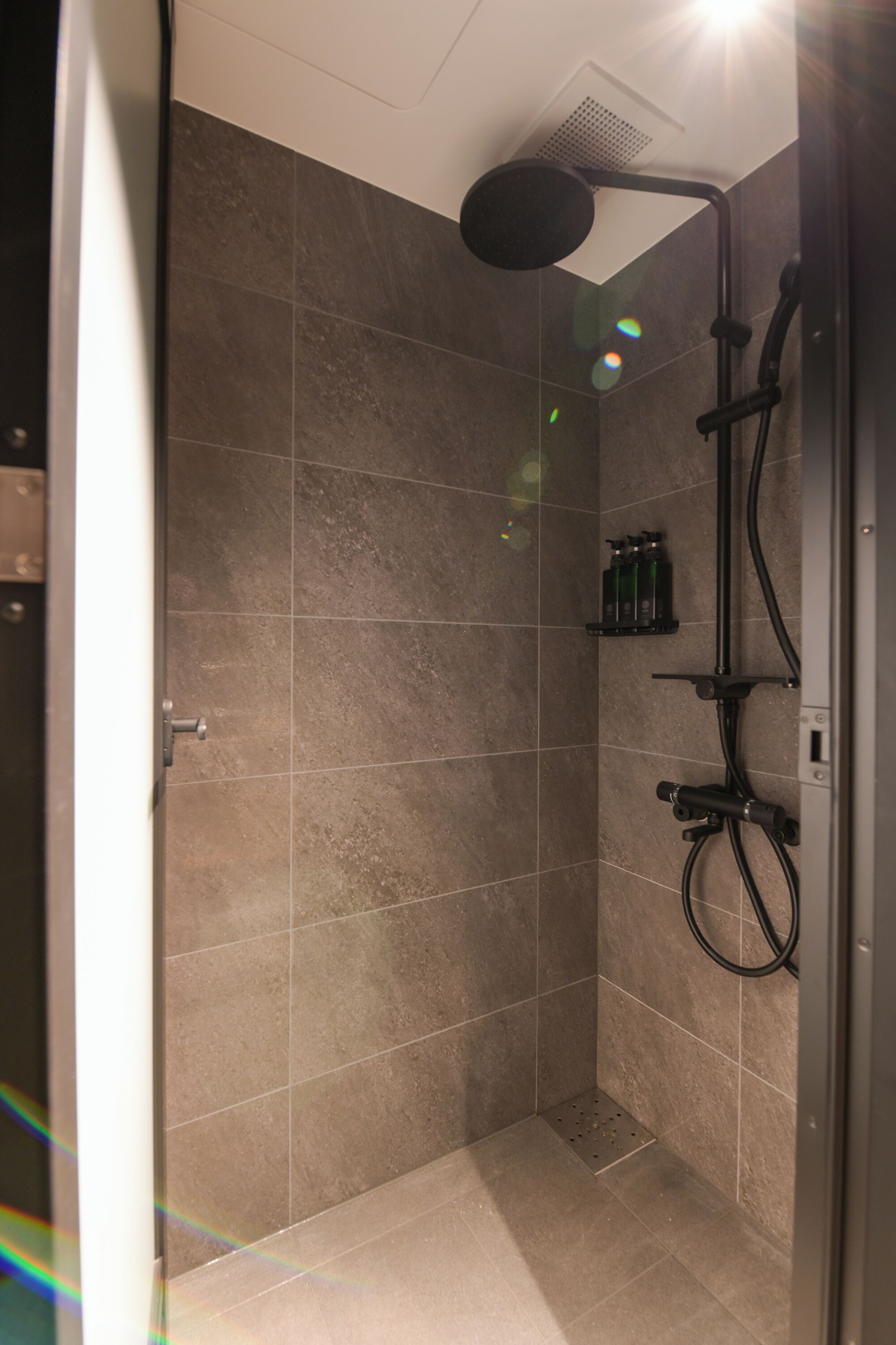 A shower area with a handheld showerhead, a wall-mounted faucet, and a control panel.