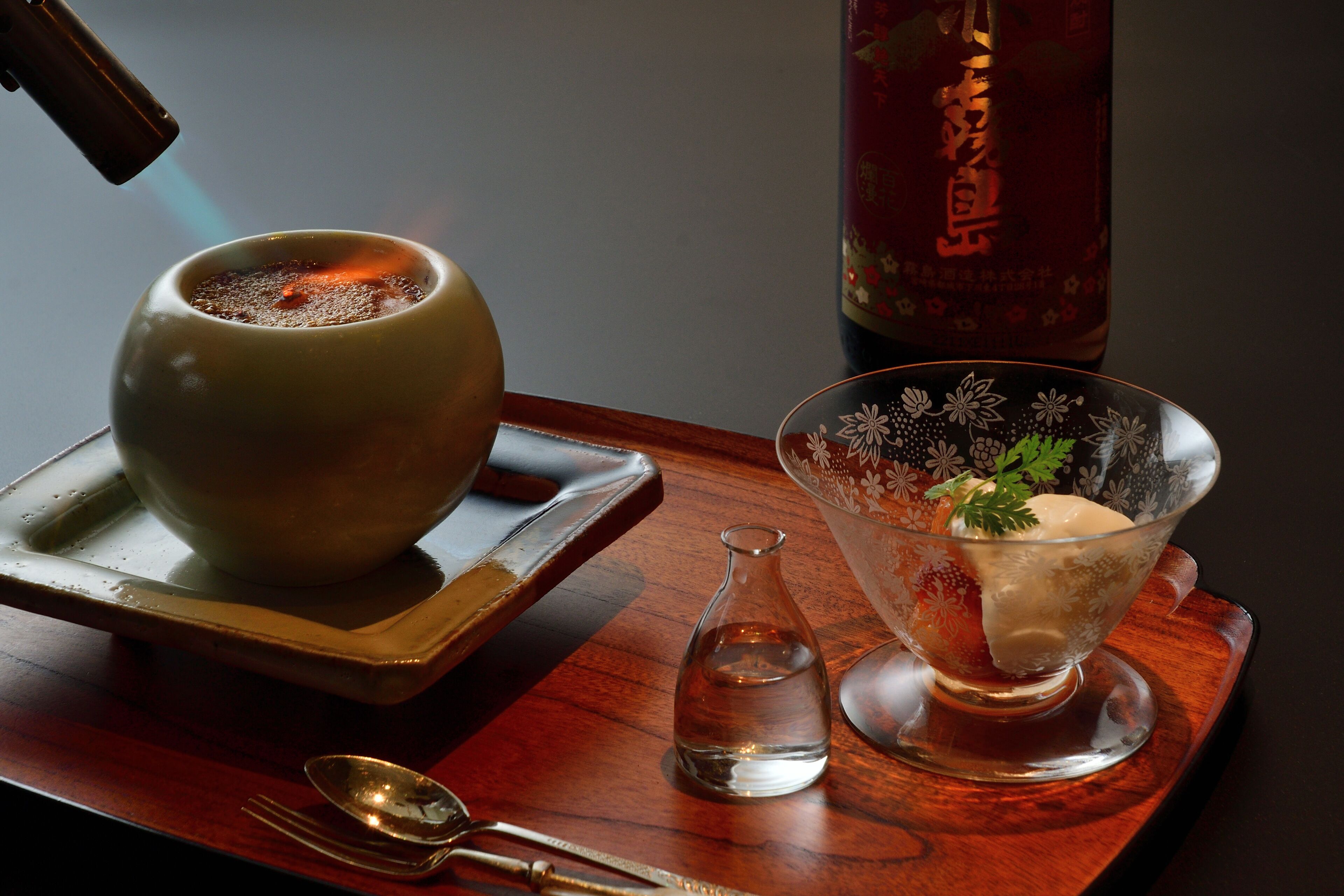 A traditional tea set with a teapot, a glass pitcher, and a bowl on a wooden tray.