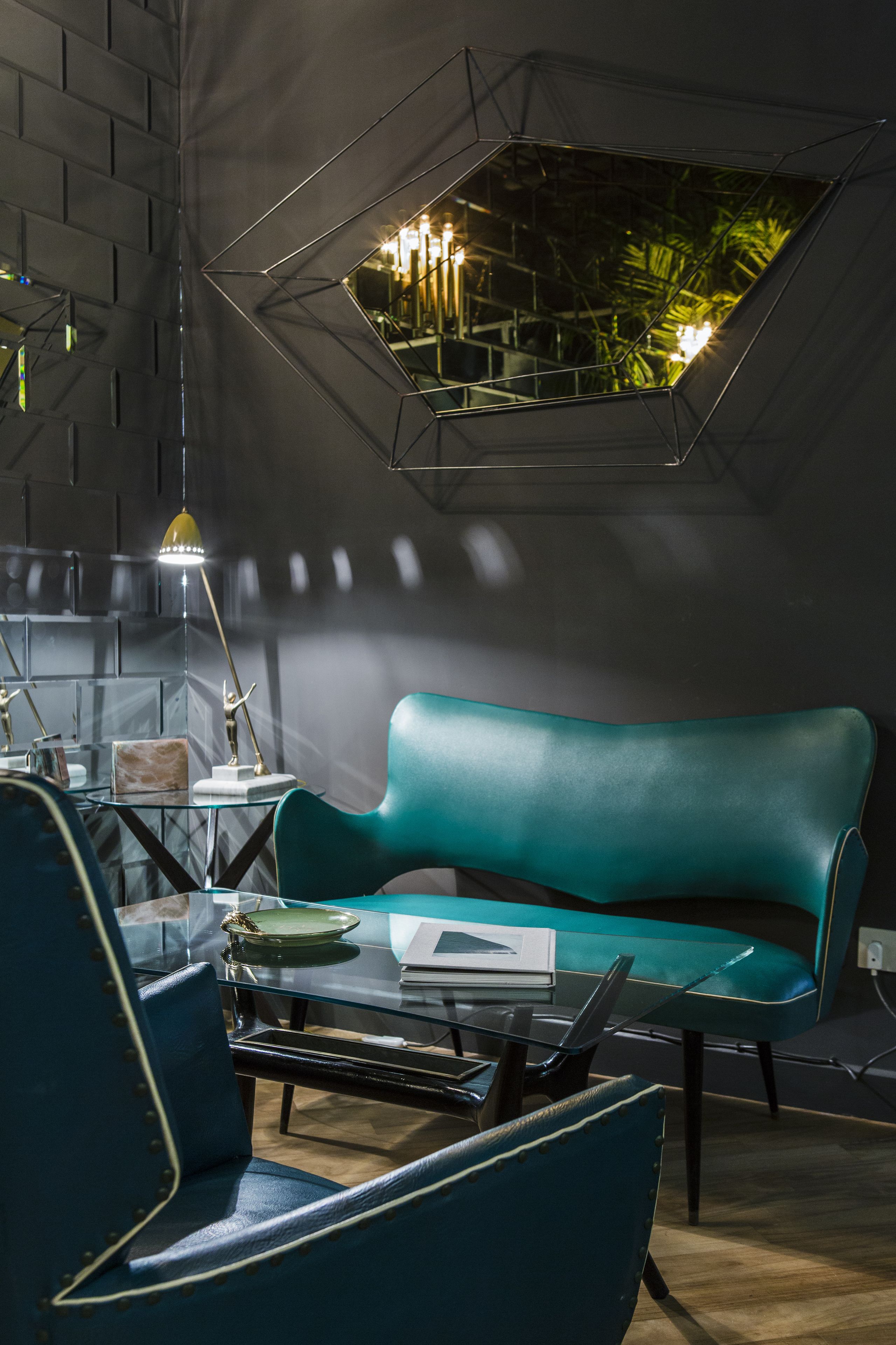Un interior moderno con un diseño de pared geométrico, un sofá color turquesa y una mesa de vidrio con una lámpara.