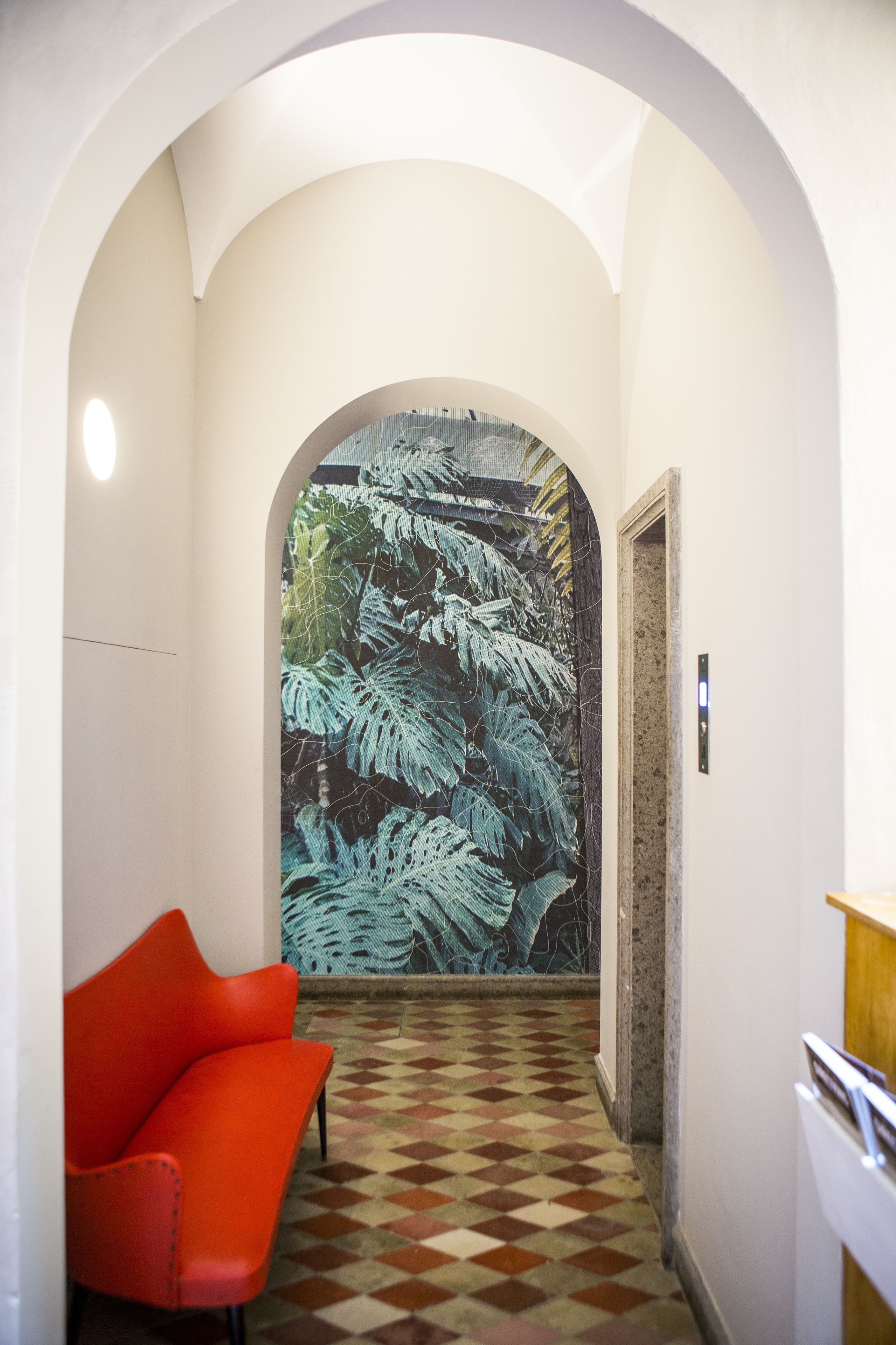 Un pasillo con piso de cuadros, una silla roja y un gran mural de helechos en la pared.