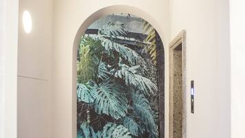 Un pasillo con piso de cuadros, una silla roja y un gran mural de helechos en la pared.