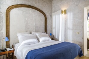 A bedroom with a large bed, a nightstand, a lamp, and a wall-mounted light fixture.
