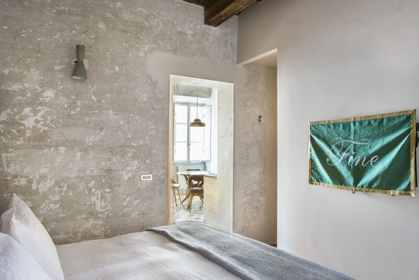 A bedroom with a concrete wall, a bed with white bedding, and a green sign with the word "Fine".