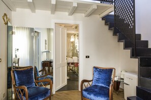 A room with two blue velvet chairs, a white door leading to a bathroom, and a staircase with a perforated railing.
