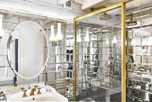 A bathroom with a large mirror, a sink with gold fixtures, and a shower area with glass walls.