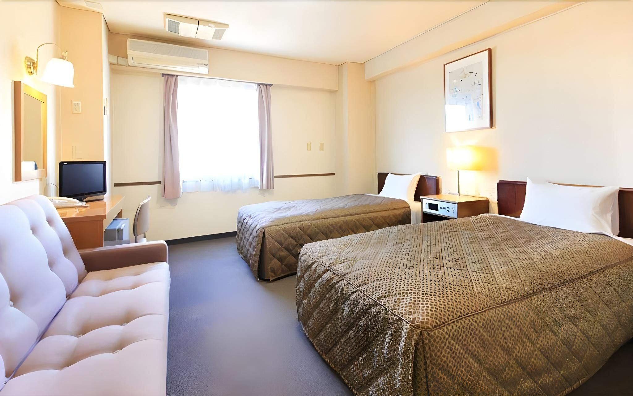 Habitación de hotel con dos camas, un escritorio, una silla, un televisor y una ventana con cortinas.