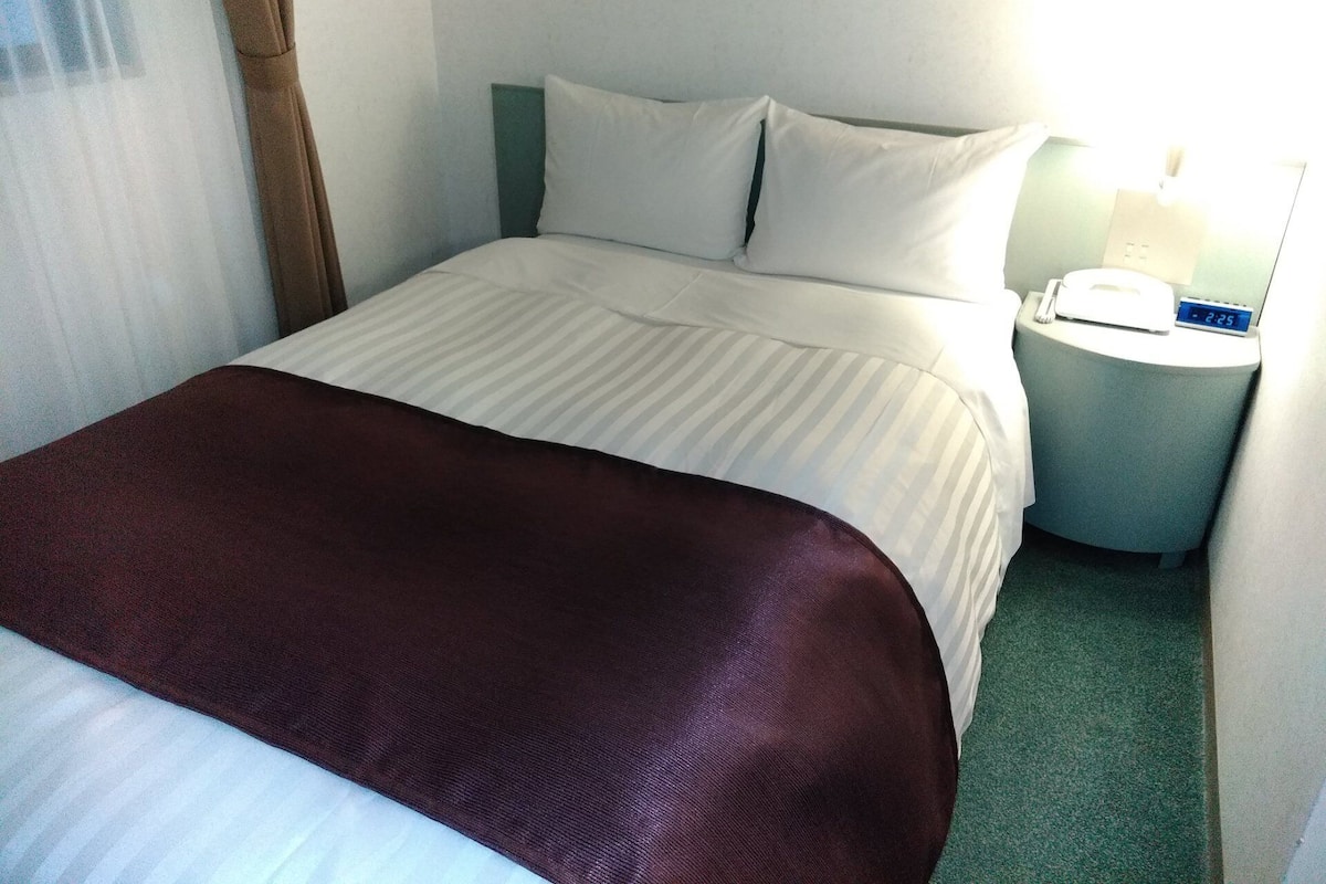 A hotel room with a bed, a bedside table with a lamp, and a clock.