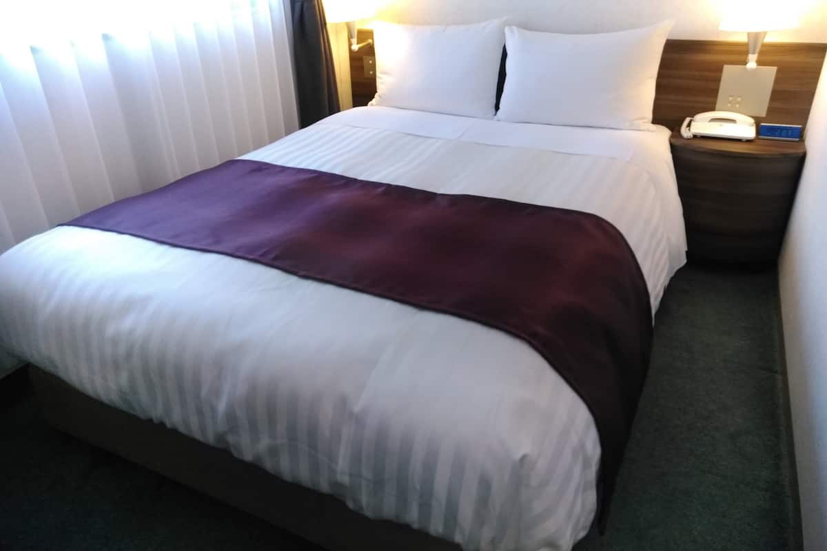 A hotel room with a bed, a nightstand with a telephone, and a wall-mounted lamp.