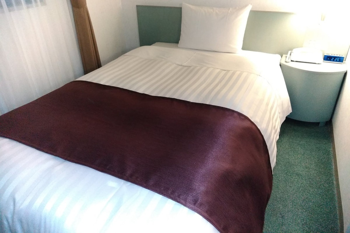 A hotel room with a bed, a nightstand, and a lamp.