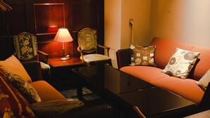 A cozy living room with a sofa, armchairs, a coffee table, and a lamp. - Van CortLandt Hotel (Aira)
