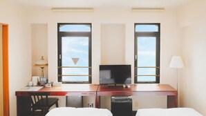 A hotel room with two beds, a desk with a television, a lamp, and a window with a view of the sky. - Van CortLandt Hotel (Aira)