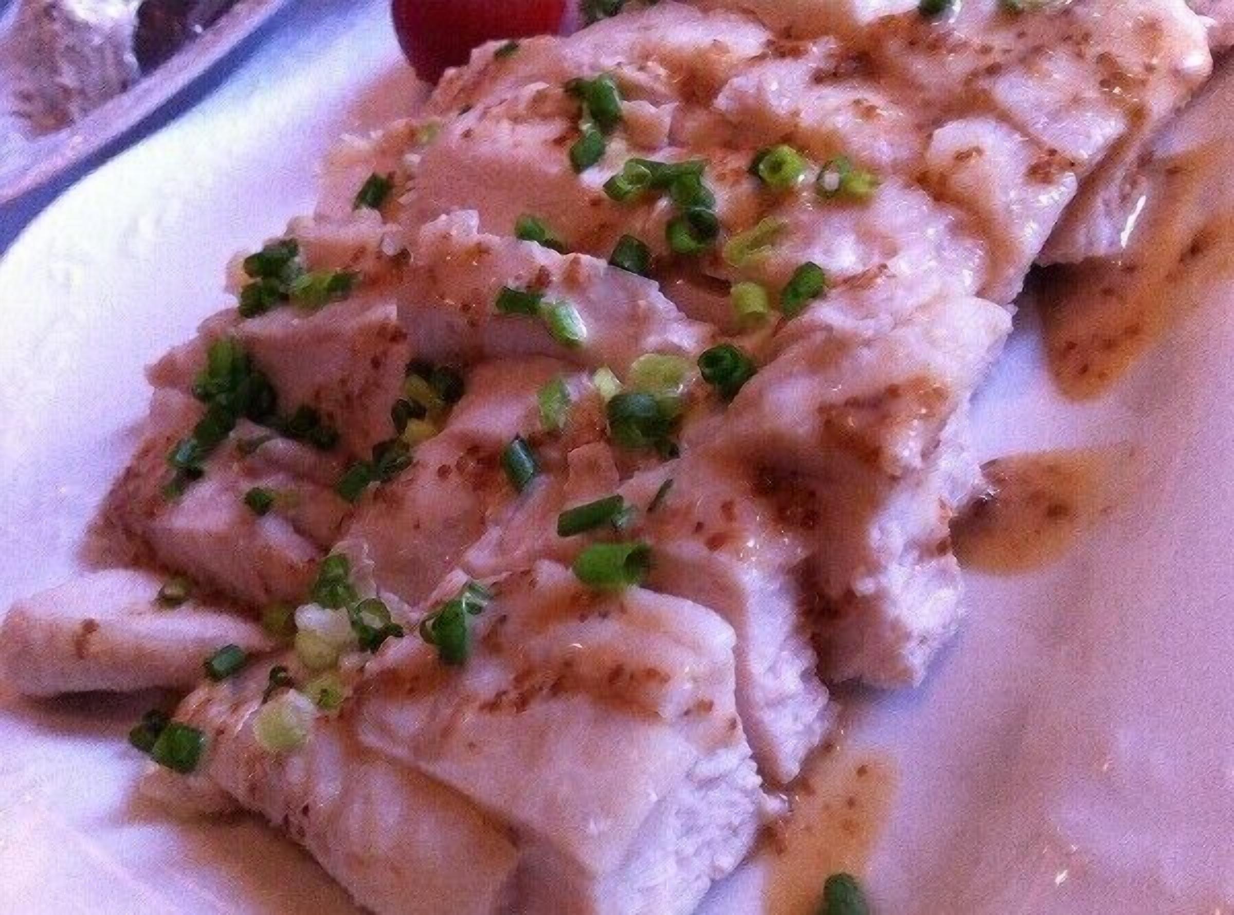 A close-up of a dish with sliced meat and green onions.