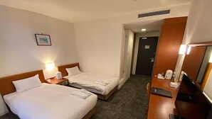 Une chambre d’hôtel avec deux lits, un bureau avec un ordinateur, une télévision et un tableau au mur.