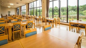 Un vaste espace dédié à la salle à manger, avec de nombreuses tables et chaises, et de grandes fenêtres donnant sur un paysage verdoyant.