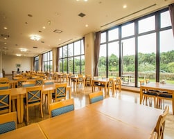 A spacious dining area with multiple tables and chairs, large windows offering a view of greenery outside.