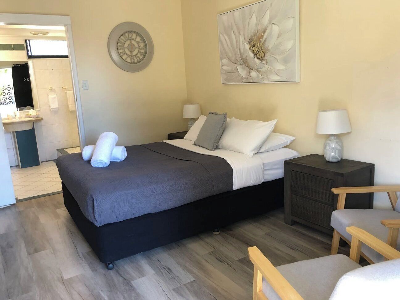 A hotel room with a bed, bedside tables, a chair, and a painting on the wall.