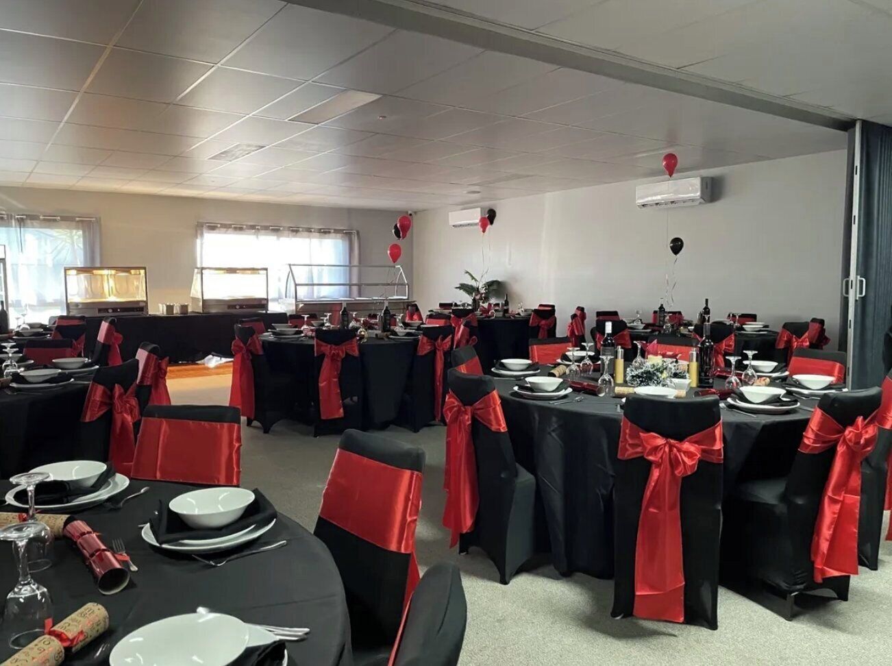 A banquet hall with tables set for a formal event, featuring black tablecloths and red sashes.