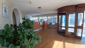 Un vestíbulo amplio con una recepción, zona de estar y grandes ventanales.