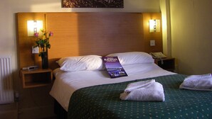 Una habitación de hotel con una cama, una mesita de noche, una lámpara, un florero con flores y un cuadro en la pared.