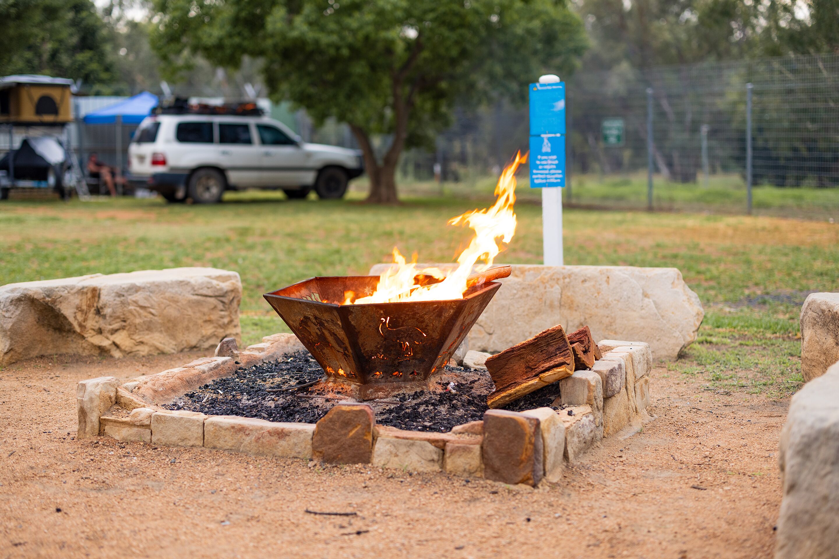 A campfire with logs and a metal fire pit surrounded by stone.