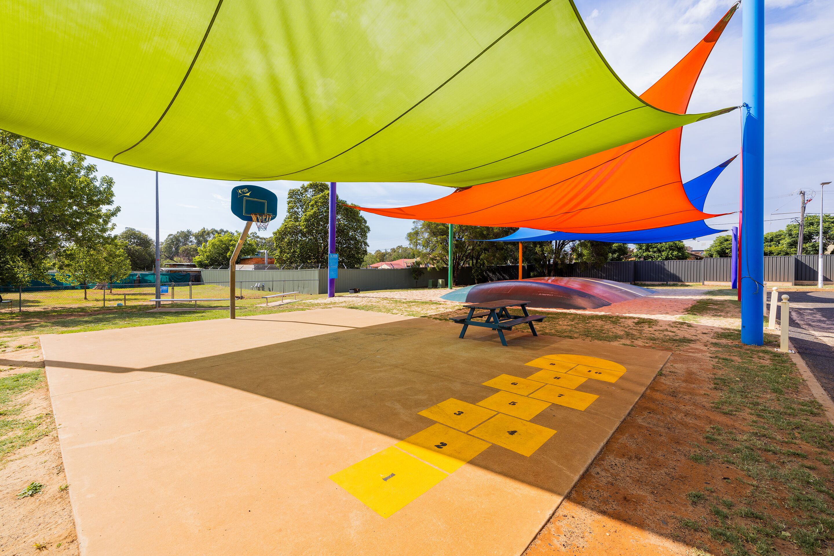 A playground with a basketball hoop, a picnic table, and a hopscotch game.