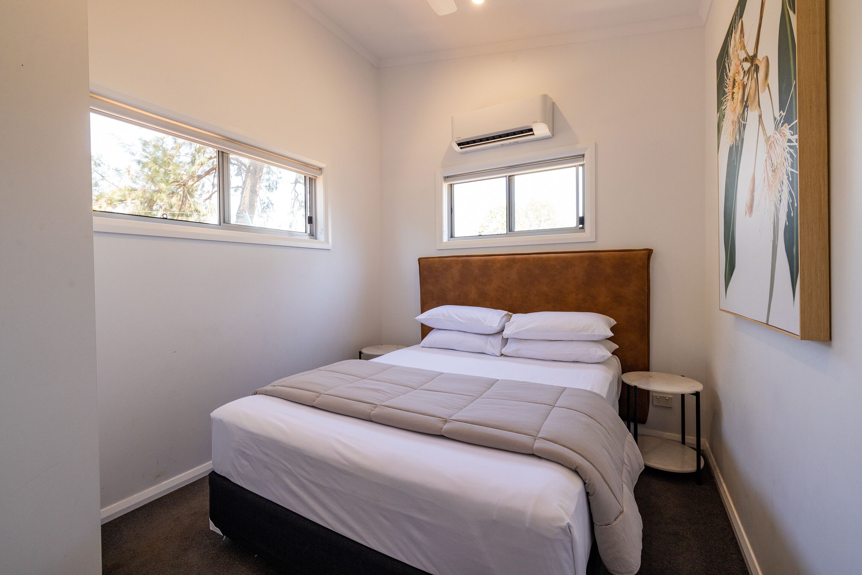 Una camera da letto con un letto, due finestre, un condizionatore, un comodino e un quadro appeso al muro.