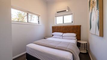 Una camera da letto con un letto, due finestre, un condizionatore, un comodino e un quadro appeso al muro.