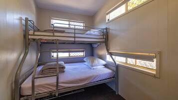 Habitación con literas y dos ventanas, cada una con una reja de metal.