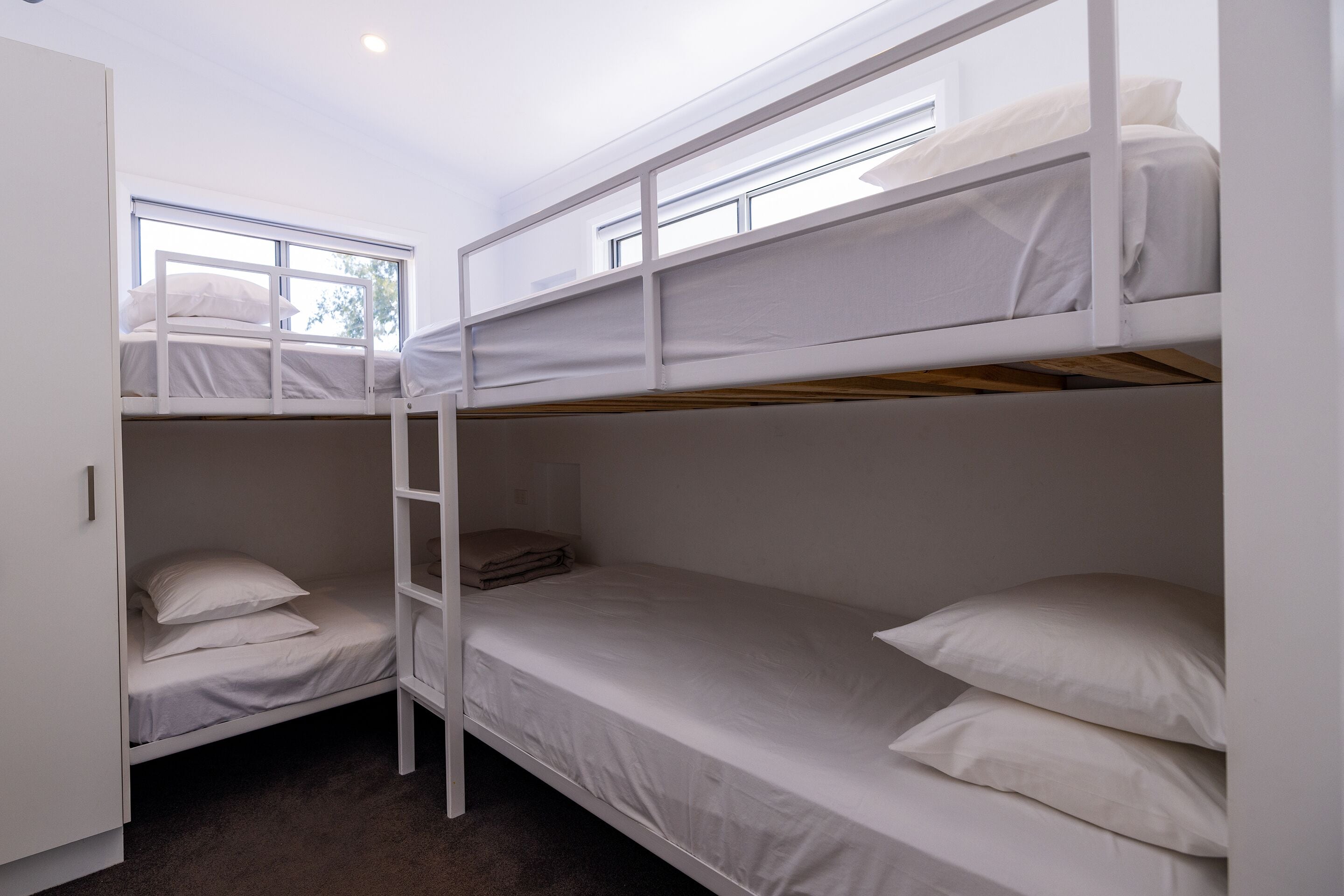 Habitación con literas, ropa de cama blanca y una escalera.