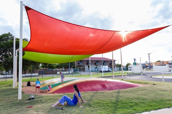 A playground with a red and green canopy, a slide, and a sandy area.