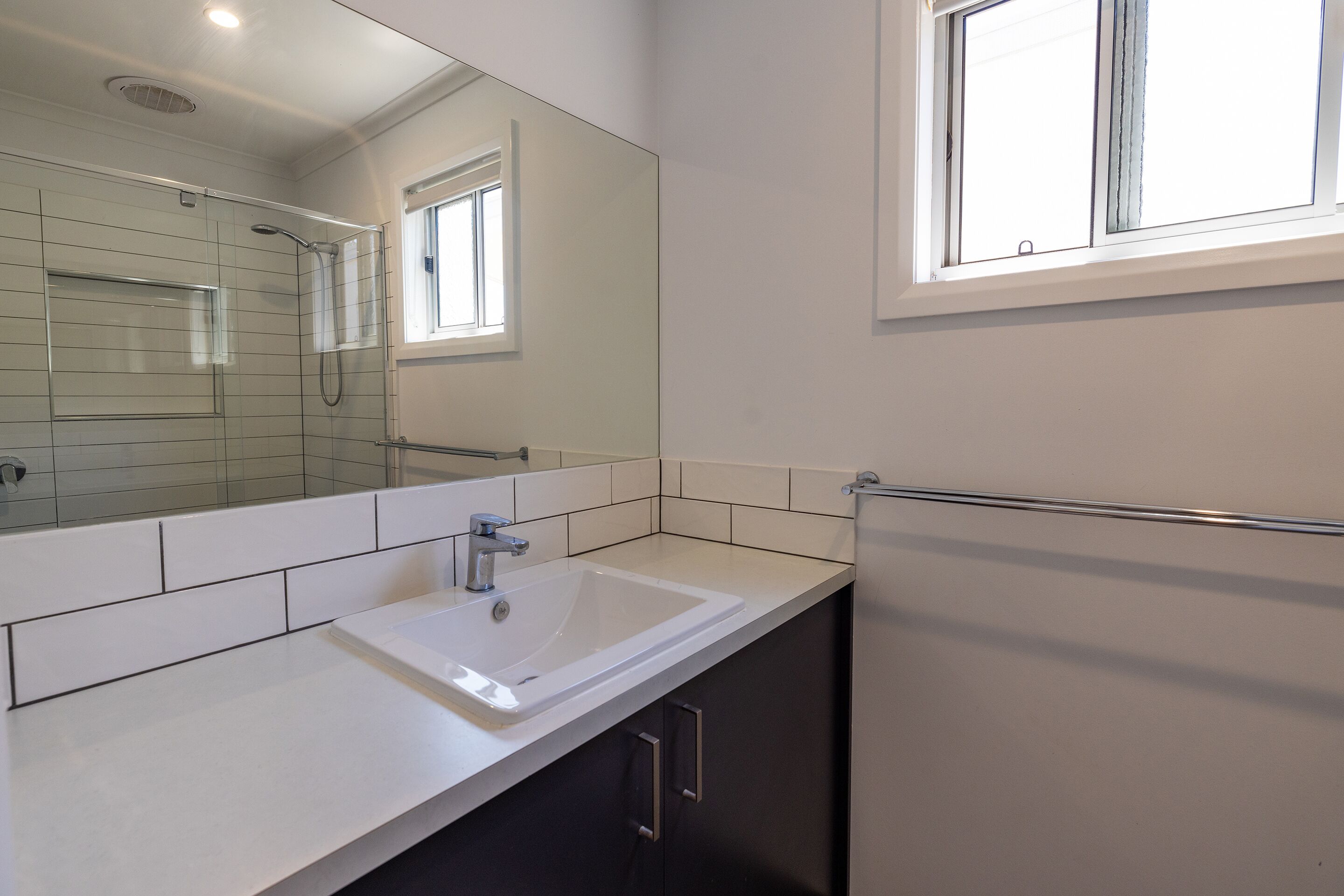 Une salle de bain moderne avec un lavabo blanc, un grand miroir et une fenêtre.