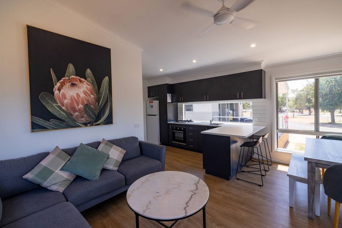 Uma sala de estar moderna com um sofá cinza, uma mesa de centro de mármore e um quadro grande de uma flor.