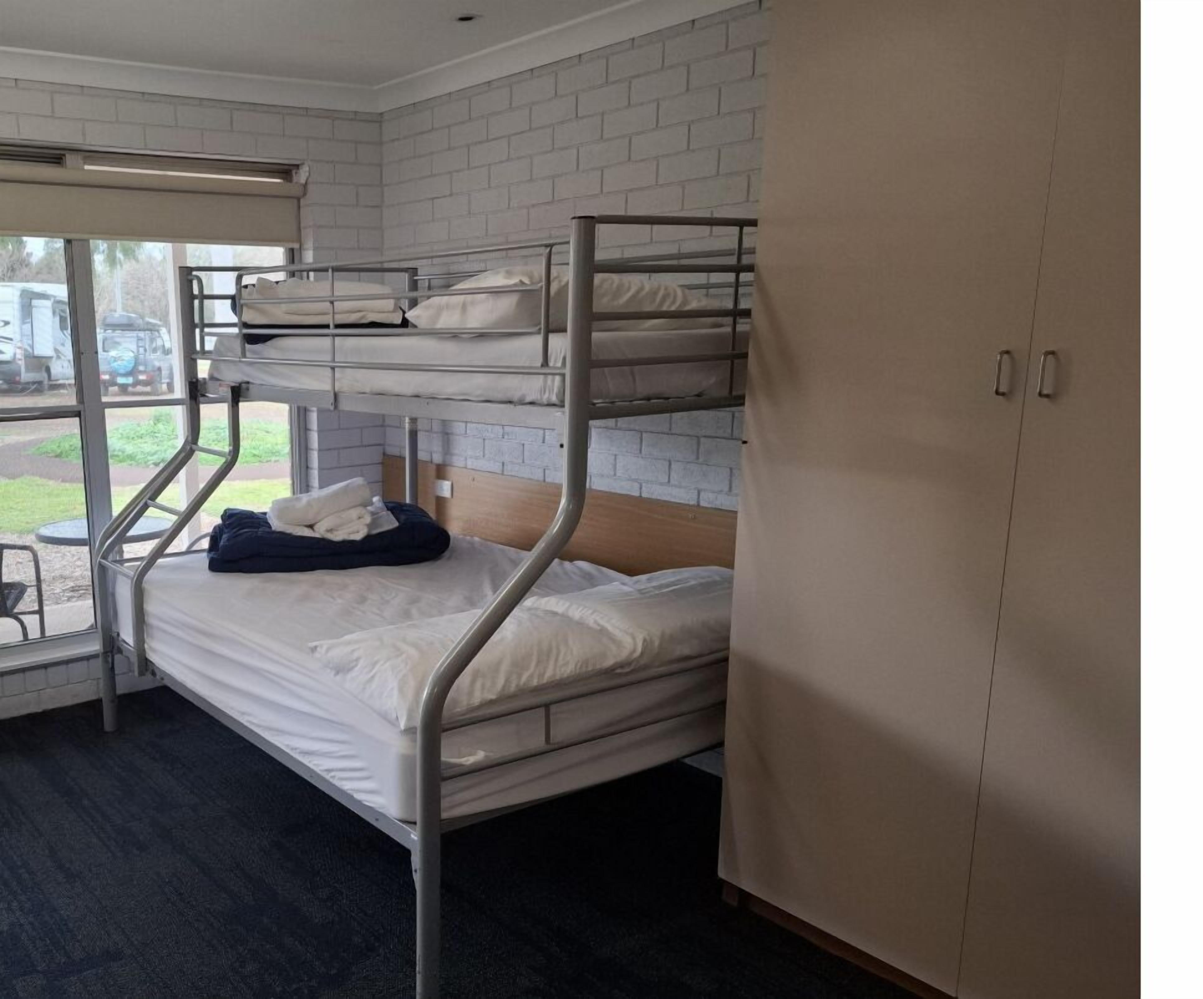 A bunk room with two bunk beds, a wooden wardrobe, and a window with a view of the outside.
