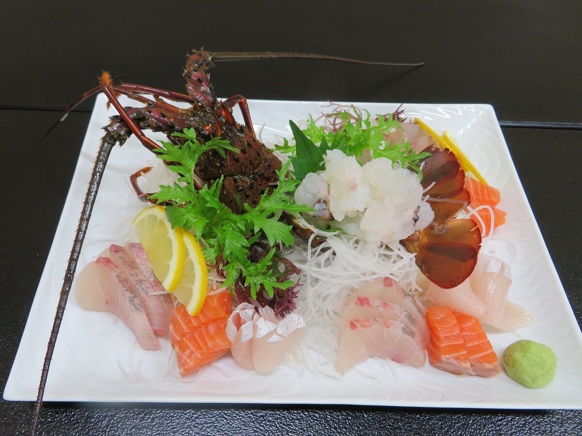 A plate of sashimi with various fish, garnishes, and a lobster tail.
