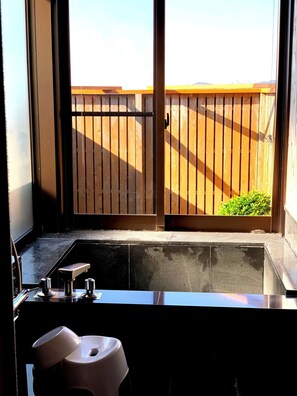 Un baño con lavamanos, inodoro y ventana que da a una cerca de madera y follaje.