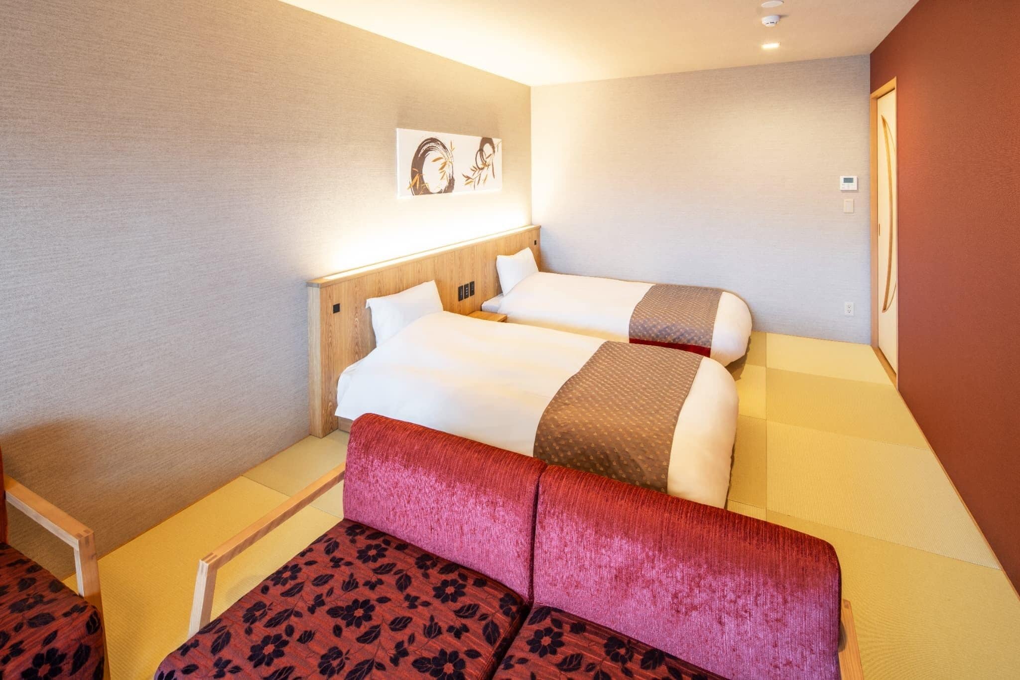 Quarto de hotel com duas camas, um sofá vermelho e uma obra de arte pendurada na parede.